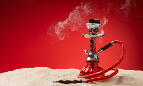 Red hookah pipe with smoke on sandy surface