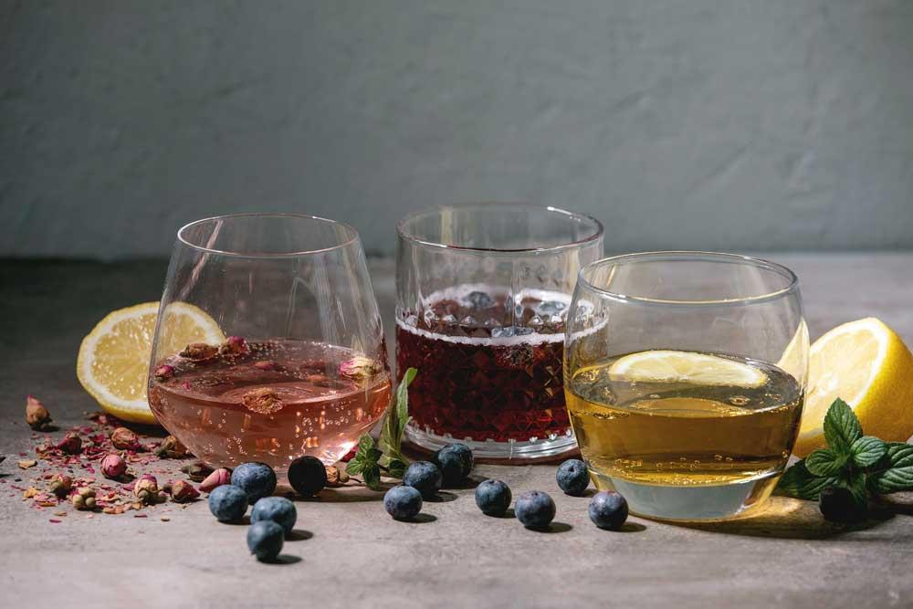 Three drinks in glasses with lemons, mint, and blueberries 