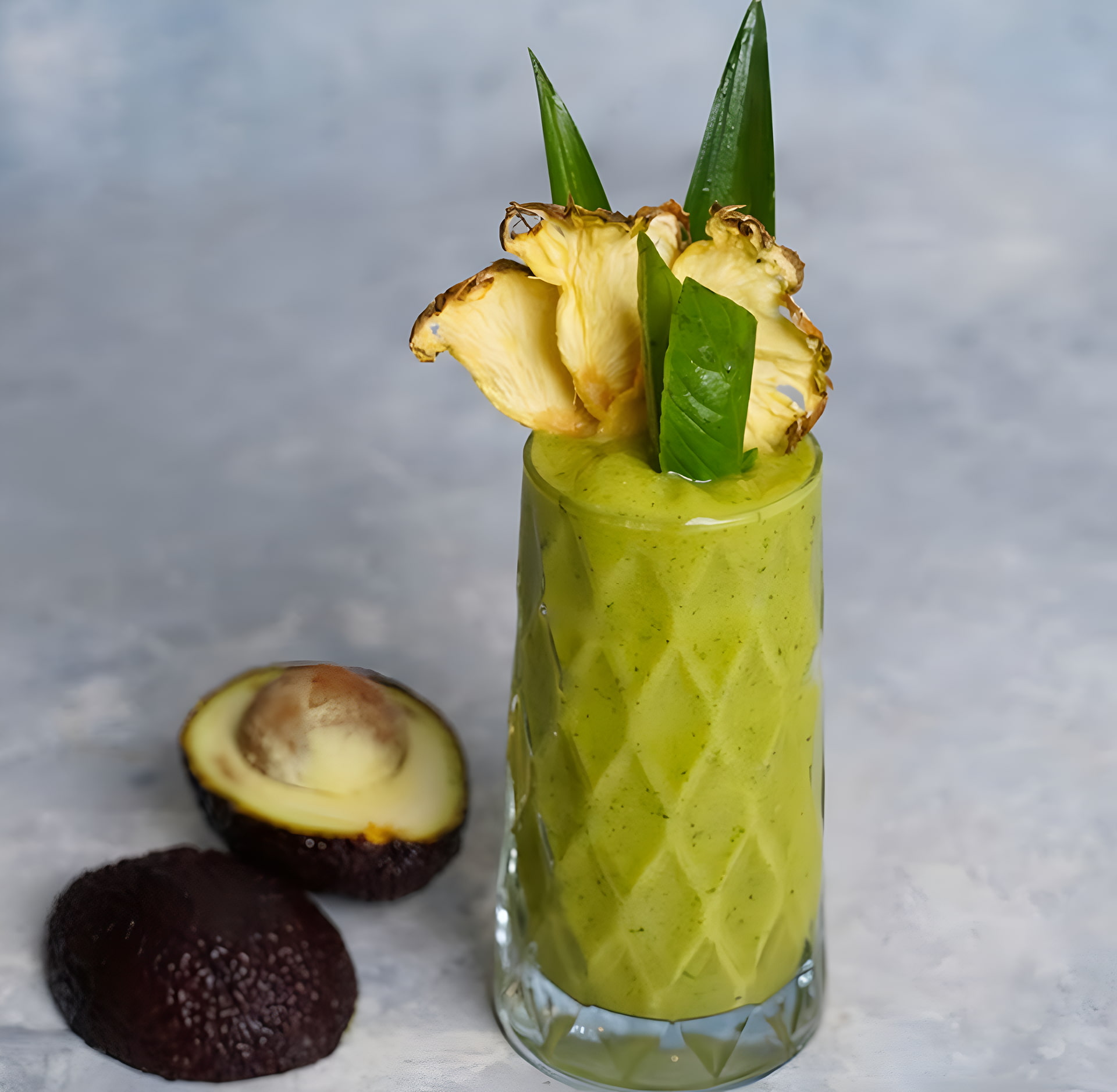 Green avocado smoothie in a tall glass garnished with dried pineapple slices and fresh leaves