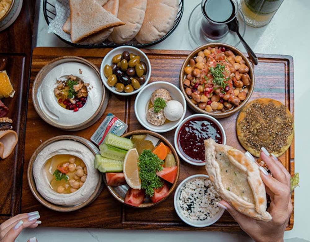 A table filled with Lebanese breakfast dishes with fruits, olives, tea, and more.