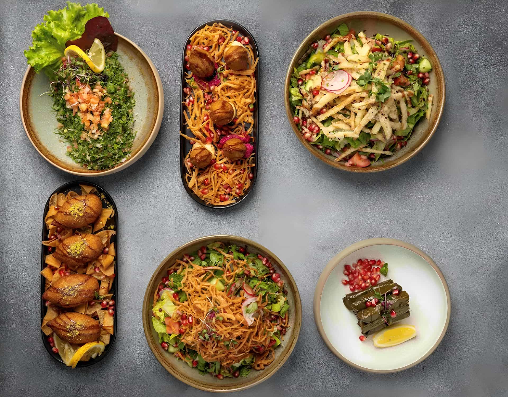 Top view of assorted Middle Eastern and fusion dishes on a dark table.