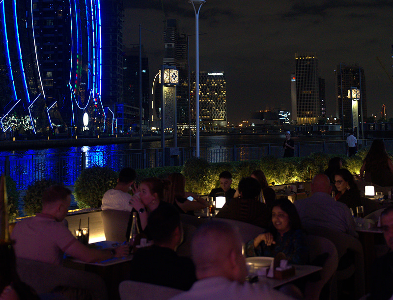 Outdoor waterfront seating at Babati Lebanese Restaurant in Business Bay Dubai with stunning views of Dubai Water Canal at night.