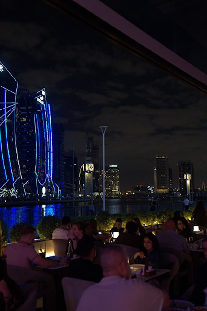 Guests on Babati's terrace at night, city lights behind