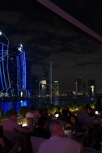 Late evening crowd at a shisha terrace on the Dubai Water Canal, city towers lit up after dark in Business Bay