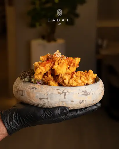 Server presenting a bowl of crispy sesame-glazed fried chicken at Babati, a canal-side lunch spot in Business Bay near Downtown Dubai